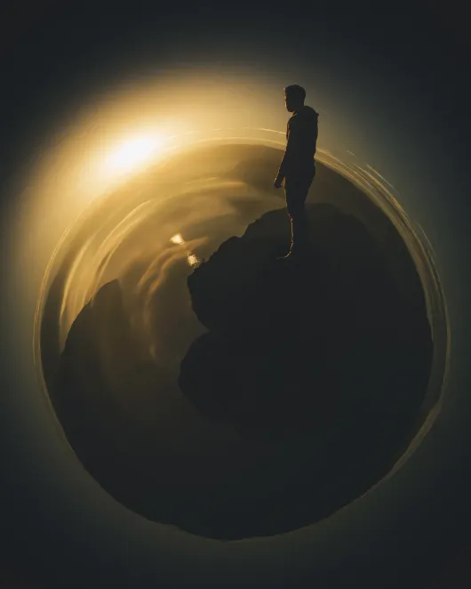 A silhouette standing on a dark sphere rimmed with gold light